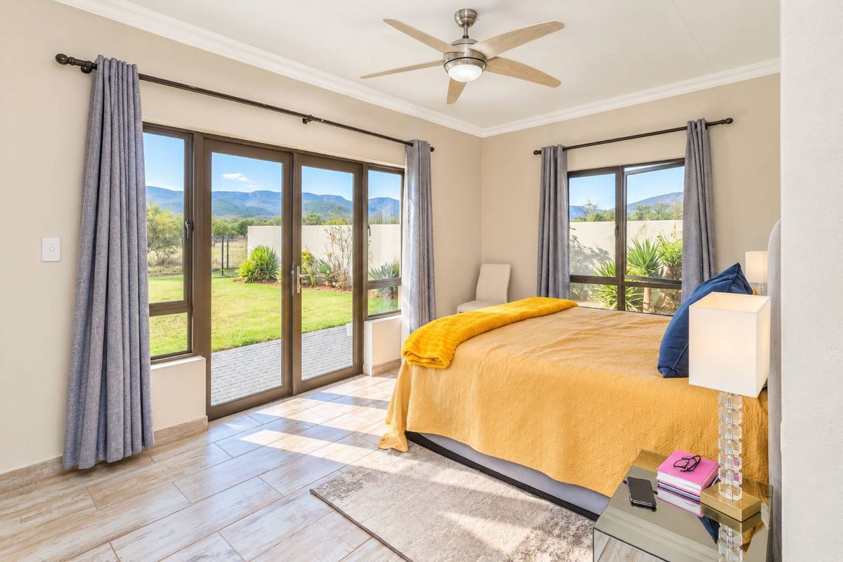 Bright bedroom featuring tiled floors, a ceiling fan, and large sliding glass doors providing direct access to the garden and mountain views.