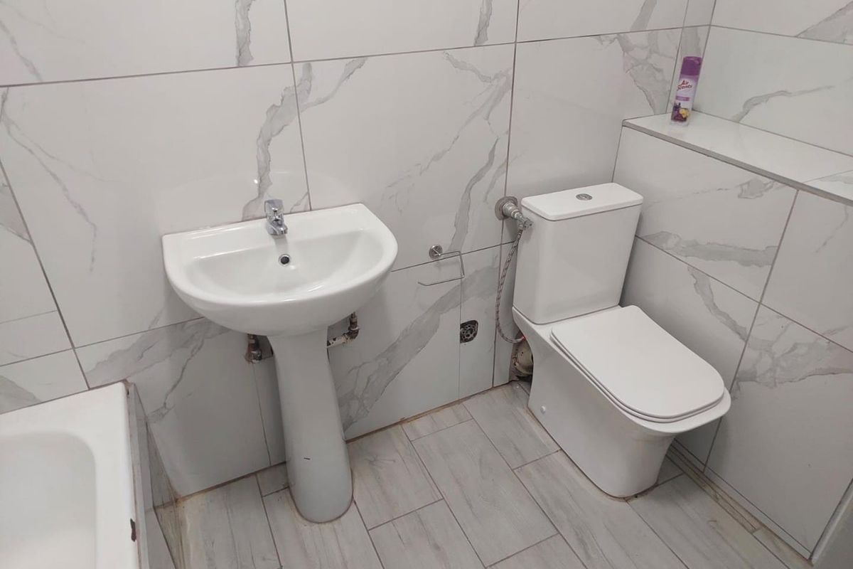 A modern bathroom featuring white marble-effect wall tiles, a pedestal basin, and a close-coupled toilet with a built-in tiled cistern ledge.