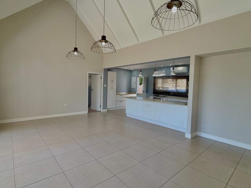 Spacious open-plan living area featuring a vaulted ceiling, tiled floors, and a modern kitchen with a central island and built-in cabinetry.