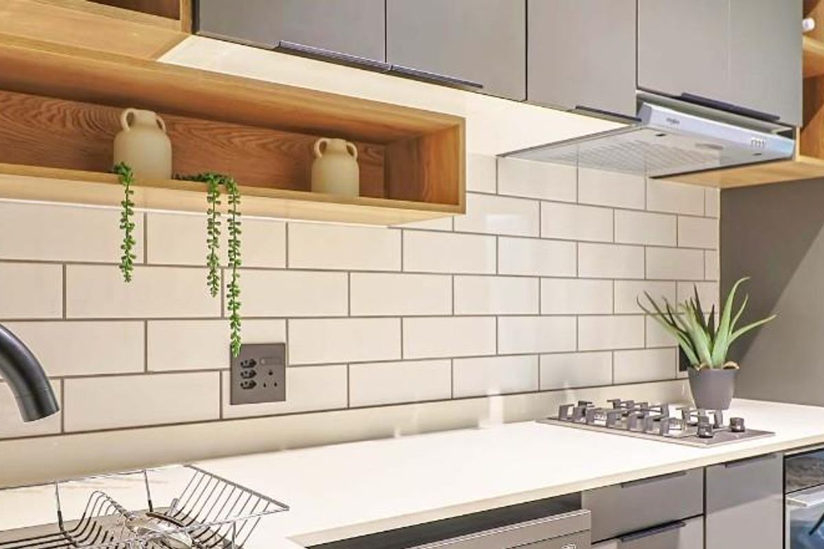 Modern kitchen featuring sleek grey cabinetry, white subway tile backsplash, integrated gas hob, extractor fan, and built-in oven with stone countertops.