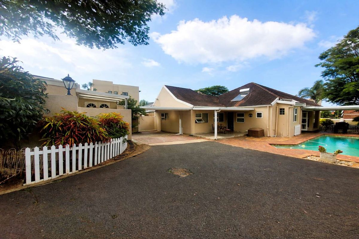 Exterior view of the property featuring a paved driveway, covered patio area, swimming pool, and tiled roof with solar water heating system.