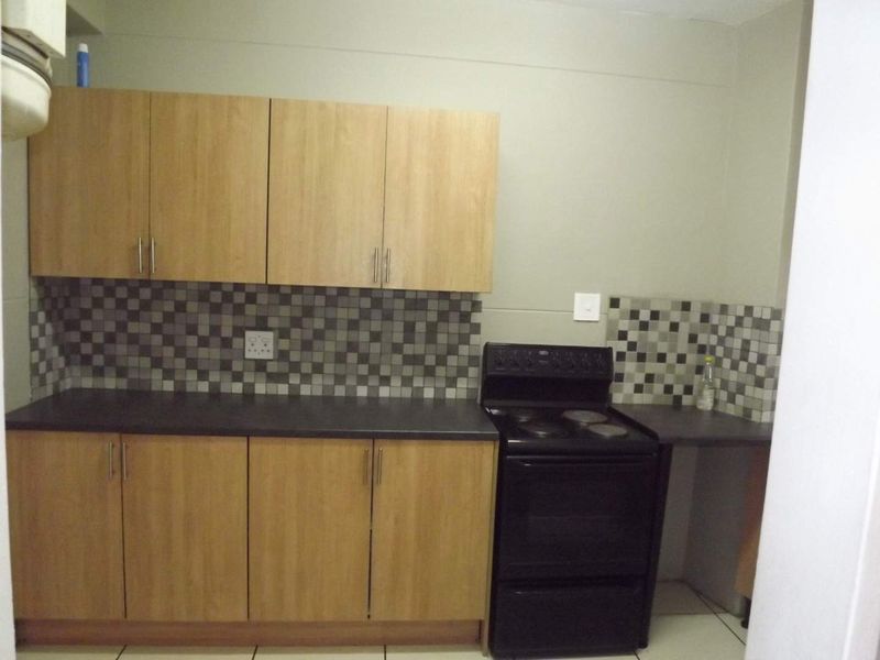 A functional kitchen featuring light wood-finish cabinetry, a dark countertop, mosaic tile backsplash, and a freestanding electric stove.