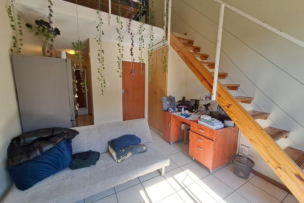 Open-plan living area featuring a staircase leading to a mezzanine level, tiled flooring, and built-in storage cupboards.