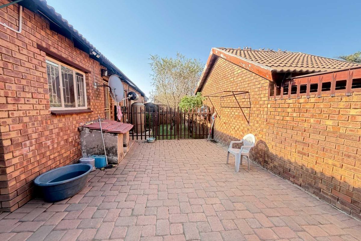 A paved rear courtyard area featuring face brick walls, a tiled roof structure, and a secure metal gate leading to the garden.