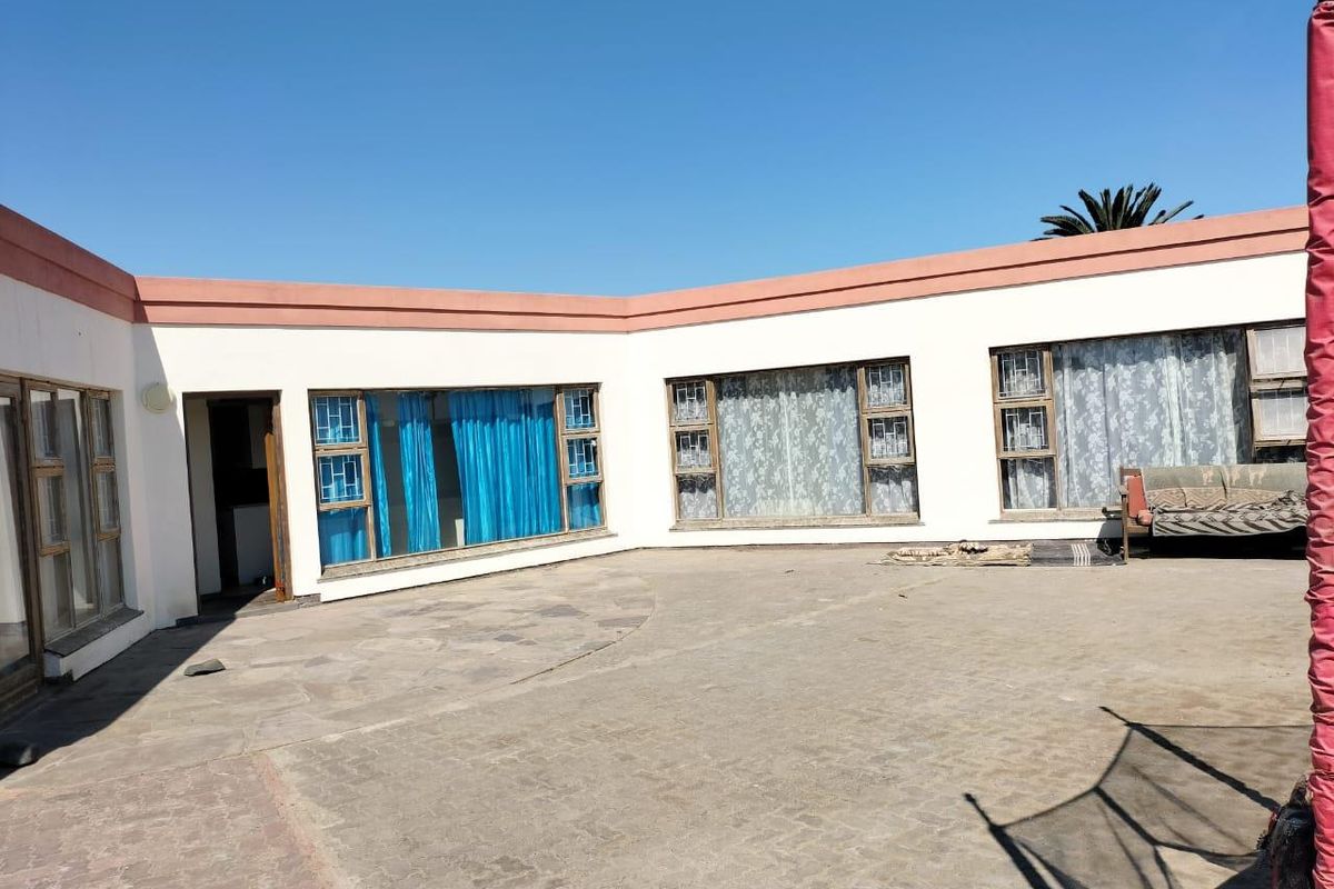 A spacious rear courtyard area featuring paved flooring and direct access to the main dwelling through large windows and a doorway.