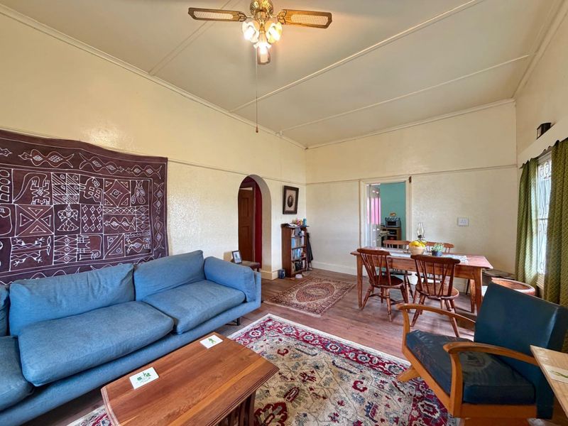 Open plan living and dining area featuring hardwood flooring, a ceiling fan, and classic architectural archways connecting to adjacent rooms.
