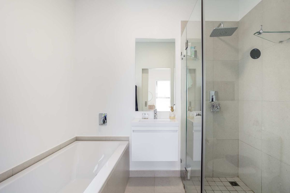 Modern bathroom featuring a built-in bathtub, wall-mounted vanity, and a spacious glass-enclosed shower with rainfall shower head and neutral tiling.