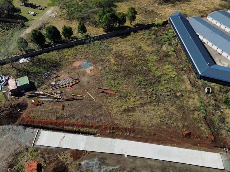 Aerial view of a vacant commercial land plot featuring a perimeter wall, a concrete slab, and adjacent metal-roofed storage structures.