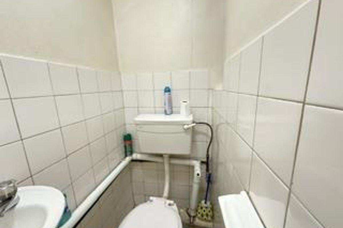 A compact bathroom featuring a standard toilet and wall-mounted basin with exposed plumbing and white ceramic wall tiles.