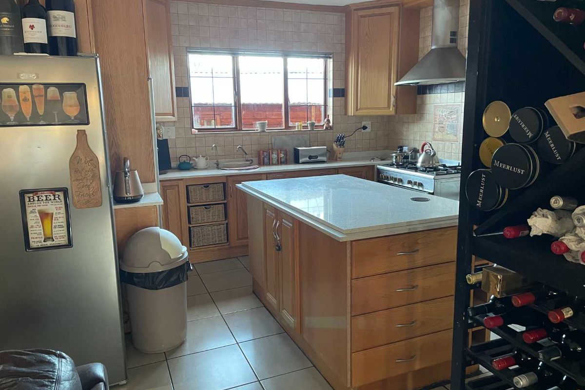 A functional kitchen featuring timber cabinetry, a central island with stone countertop, stainless steel extractor fan, gas hob, and tiled flooring.