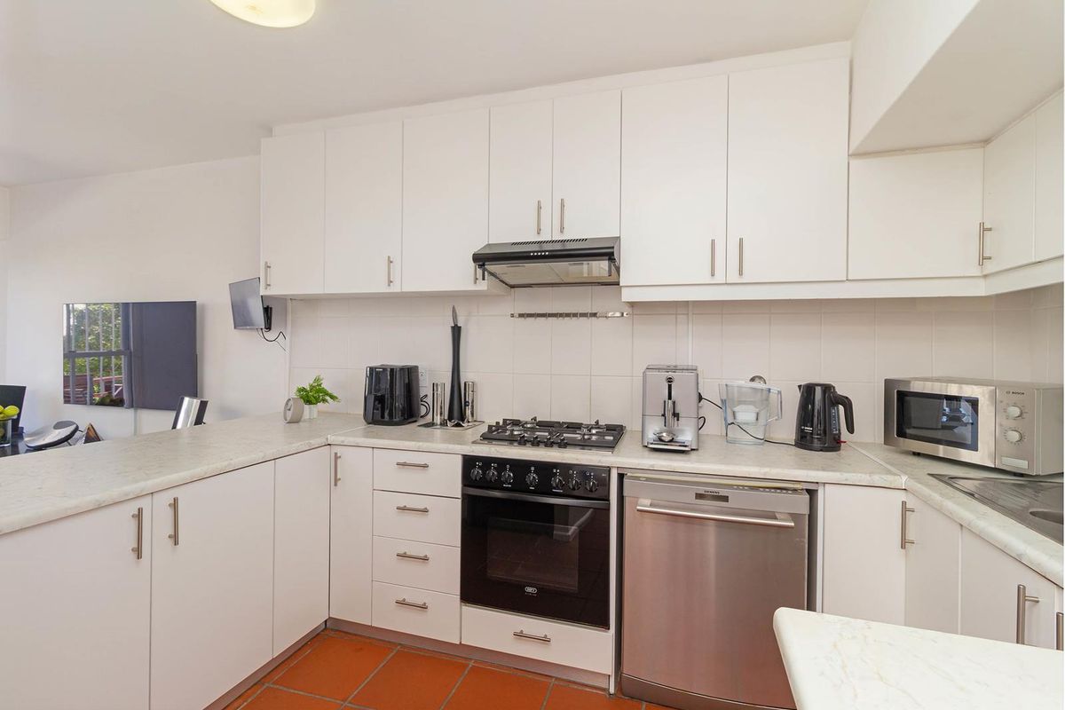 A functional kitchen featuring white cabinetry, gas hob, built-in oven, extractor fan, and terracotta floor tiles, offering a clean and practical workspace.