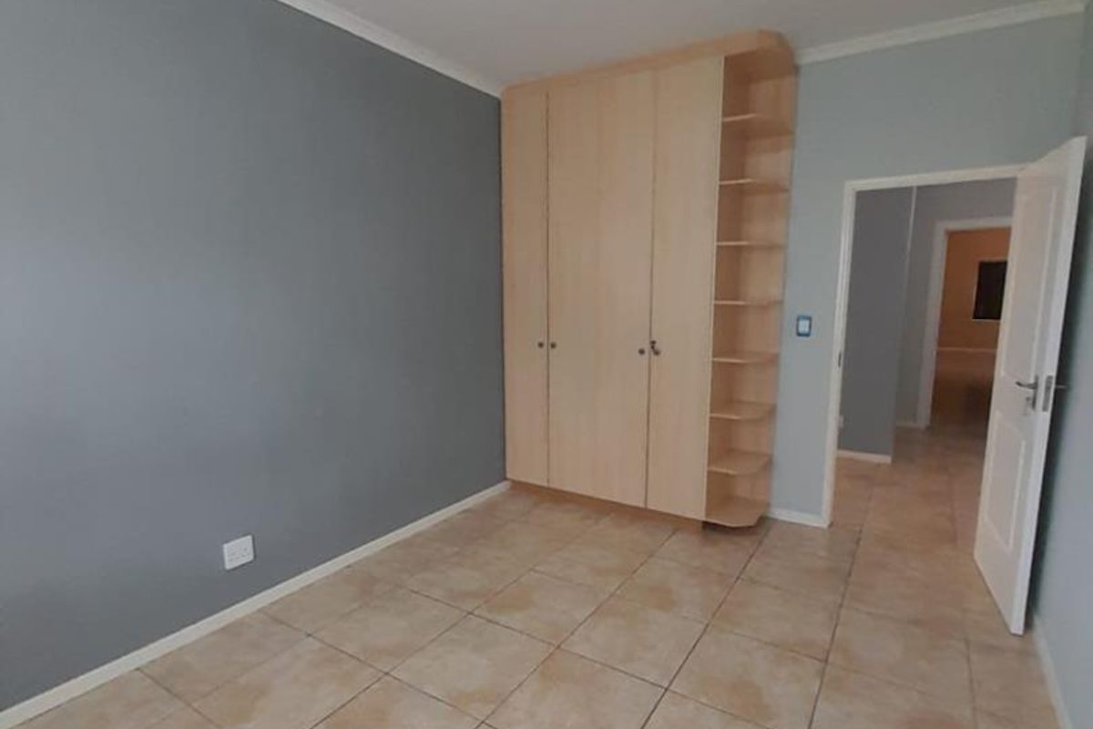 A bedroom featuring tiled flooring, built-in wooden cupboards with integrated shelving, and a neutral grey accent wall.