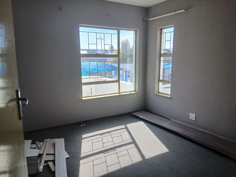 An empty bedroom featuring steel-framed windows with security bars, requiring flooring completion and minor cosmetic wall repairs.