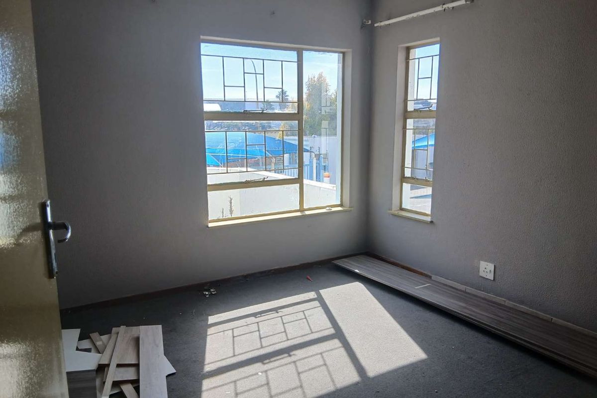 An empty bedroom featuring steel-framed windows with security bars, requiring flooring completion and minor cosmetic wall repairs.