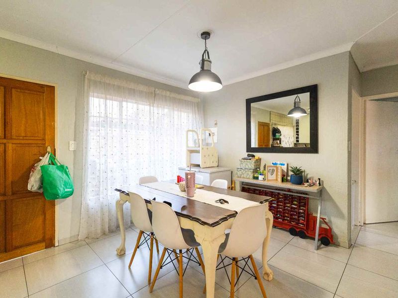 A functional dining area featuring tiled flooring, a central pendant light fixture, and a classic timber door, providing a practical space for family meals.