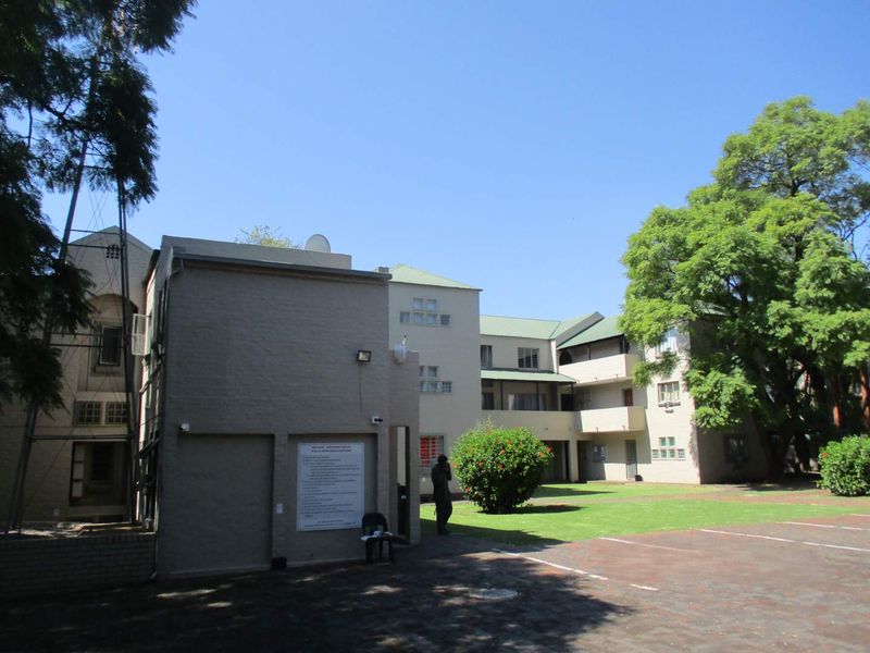 Exterior view of the apartment complex featuring a paved driveway, landscaped garden area, and multi-story building facade.