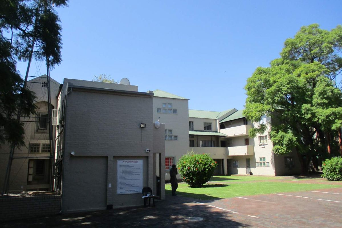 Exterior view of the apartment complex featuring a paved driveway, landscaped garden area, and multi-story building facade.