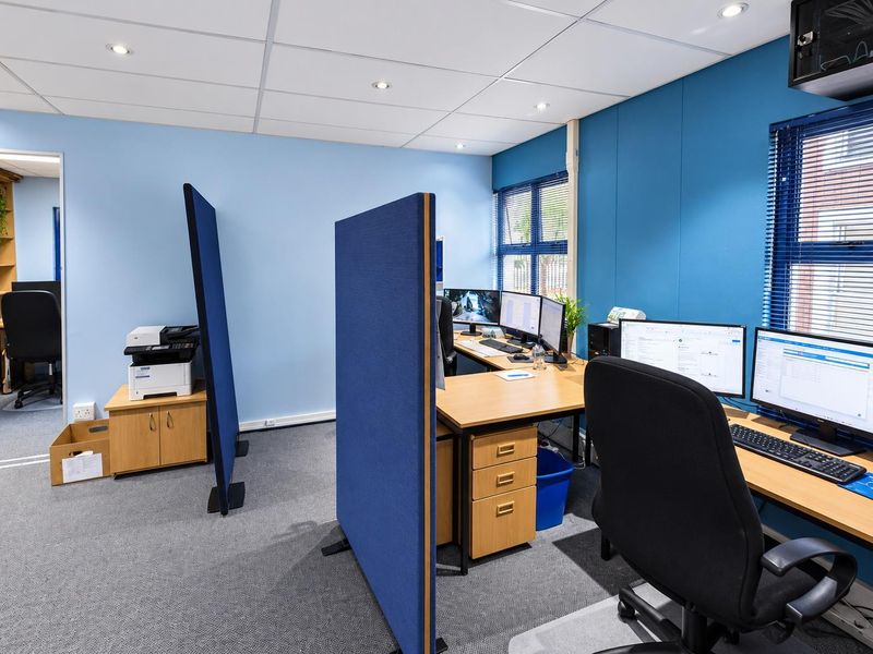 A functional office space featuring a suspended ceiling with recessed lighting, built-in shelving, and large windows with venetian blinds.