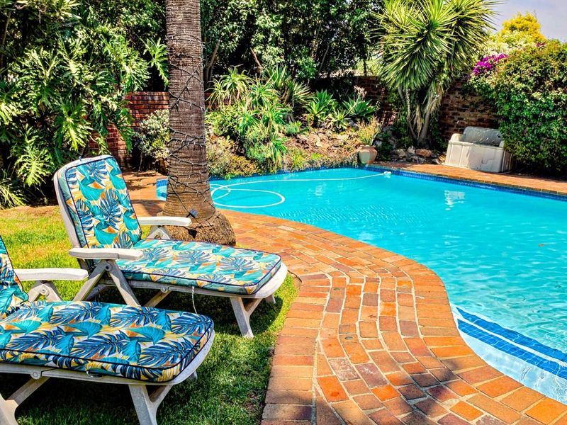 A well-maintained swimming pool area featuring brick coping, surrounded by established garden landscaping and a brick boundary wall.