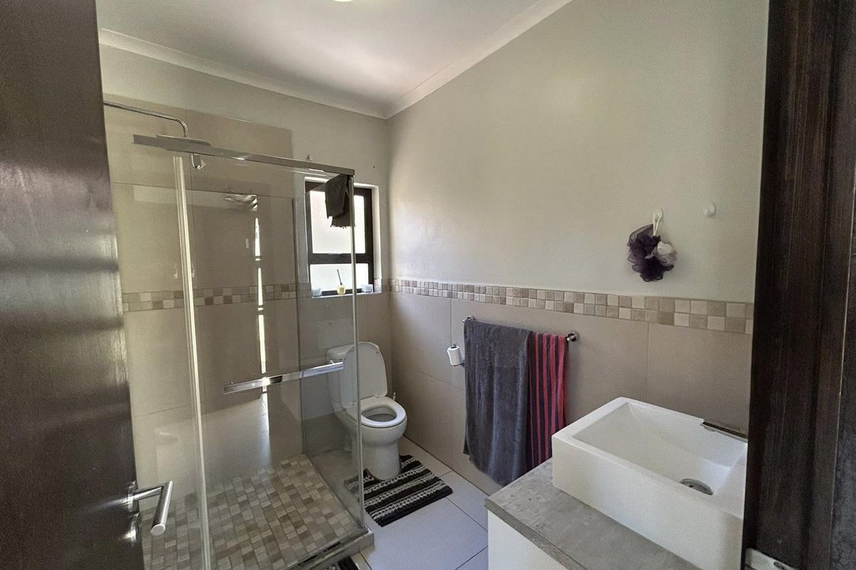 Modern bathroom featuring a glass-enclosed shower, a contemporary vessel sink on a vanity, and neutral wall tiling with a decorative mosaic border.