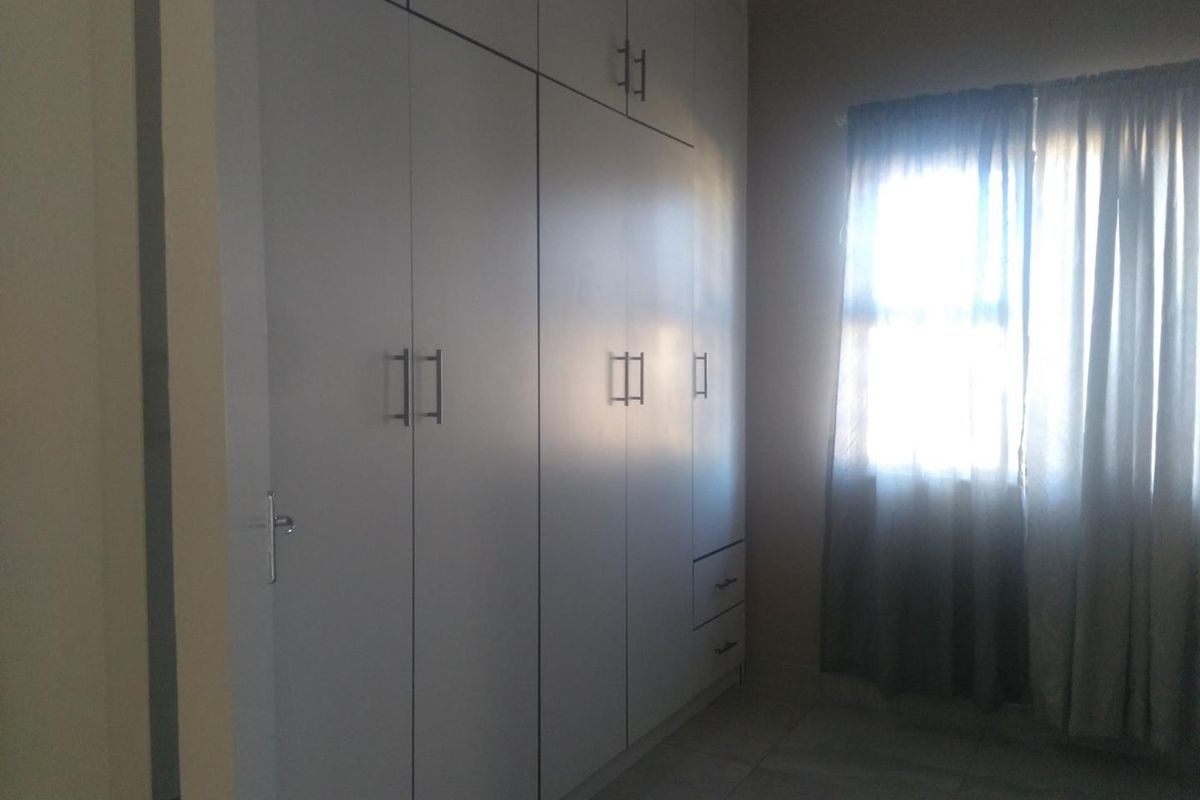 A clean, empty bedroom featuring modern built-in cupboards with sleek handles and neutral tiled flooring, offering a bright and functional living space.