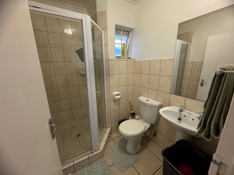 A functional bathroom featuring a corner shower enclosure, pedestal basin, and toilet with neutral wall and floor tiling.