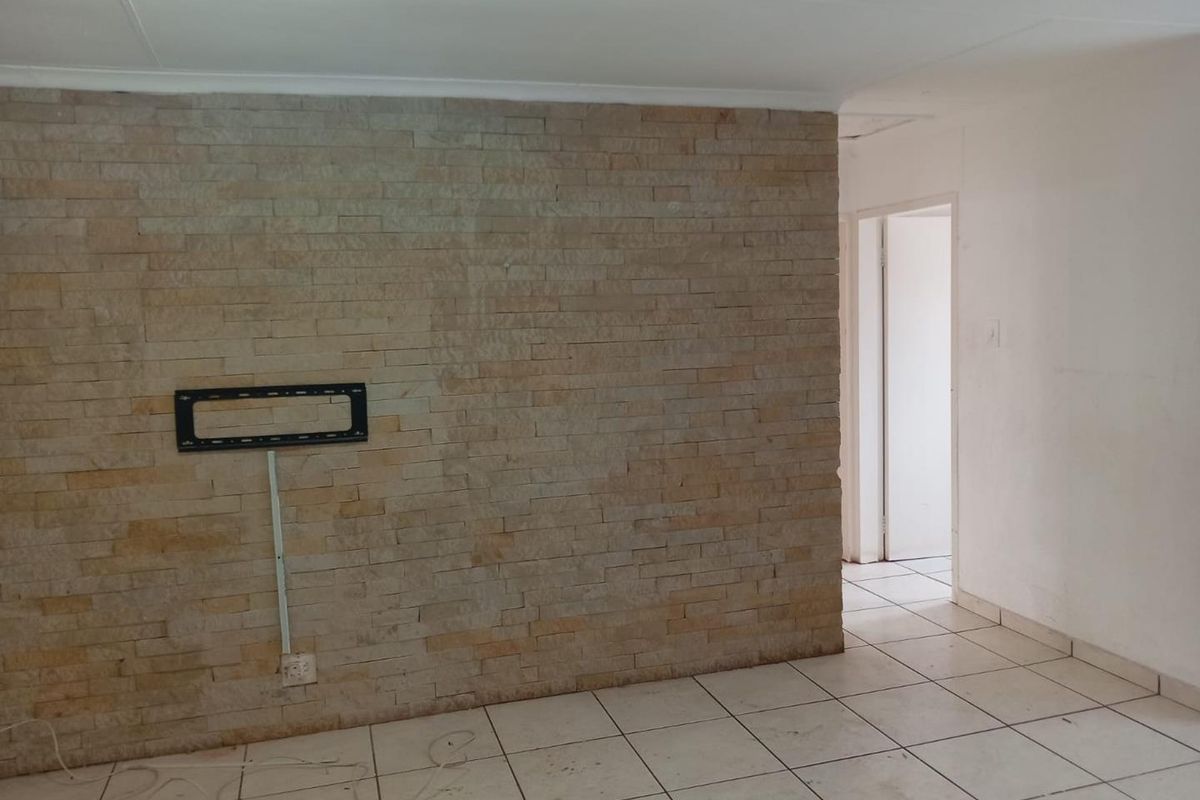 Living area featuring a textured stone feature wall, ceramic floor tiles, and a wall-mounted television bracket.