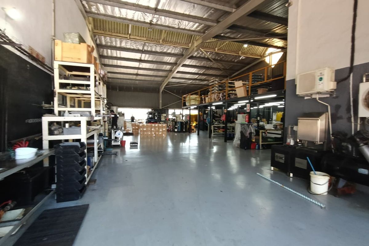 Spacious industrial warehouse featuring high ceilings with exposed steel trusses, a functional mezzanine level, and durable epoxy-coated concrete flooring.