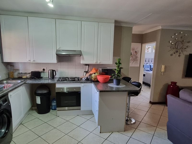 Open plan kitchen and living area featuring white cabinetry, laminate countertops, built-in oven, hob, and tiled flooring throughout the space.