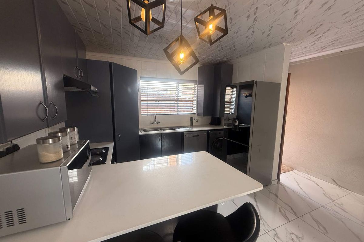 Modern kitchen featuring dark cabinetry, white stone countertops, a breakfast bar, and contemporary pendant lighting with marble-look floor tiles.
