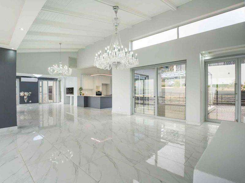 Spacious open-plan living area featuring high vaulted ceilings, polished marble-look tile flooring, elegant crystal chandeliers, and seamless access to the outdoor patio.