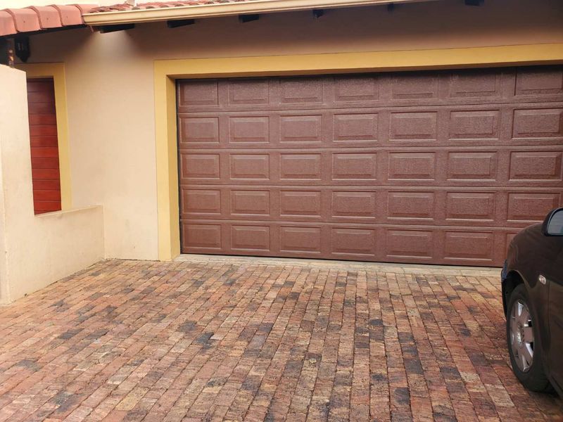 A well-maintained single garage featuring a brown sectional door and a brick-paved driveway.