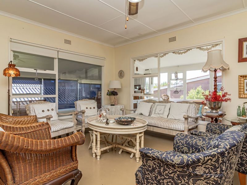 A bright living room featuring large sliding glass windows, an exposed beam ceiling, and a ceiling fan, offering a comfortable and well-lit space.