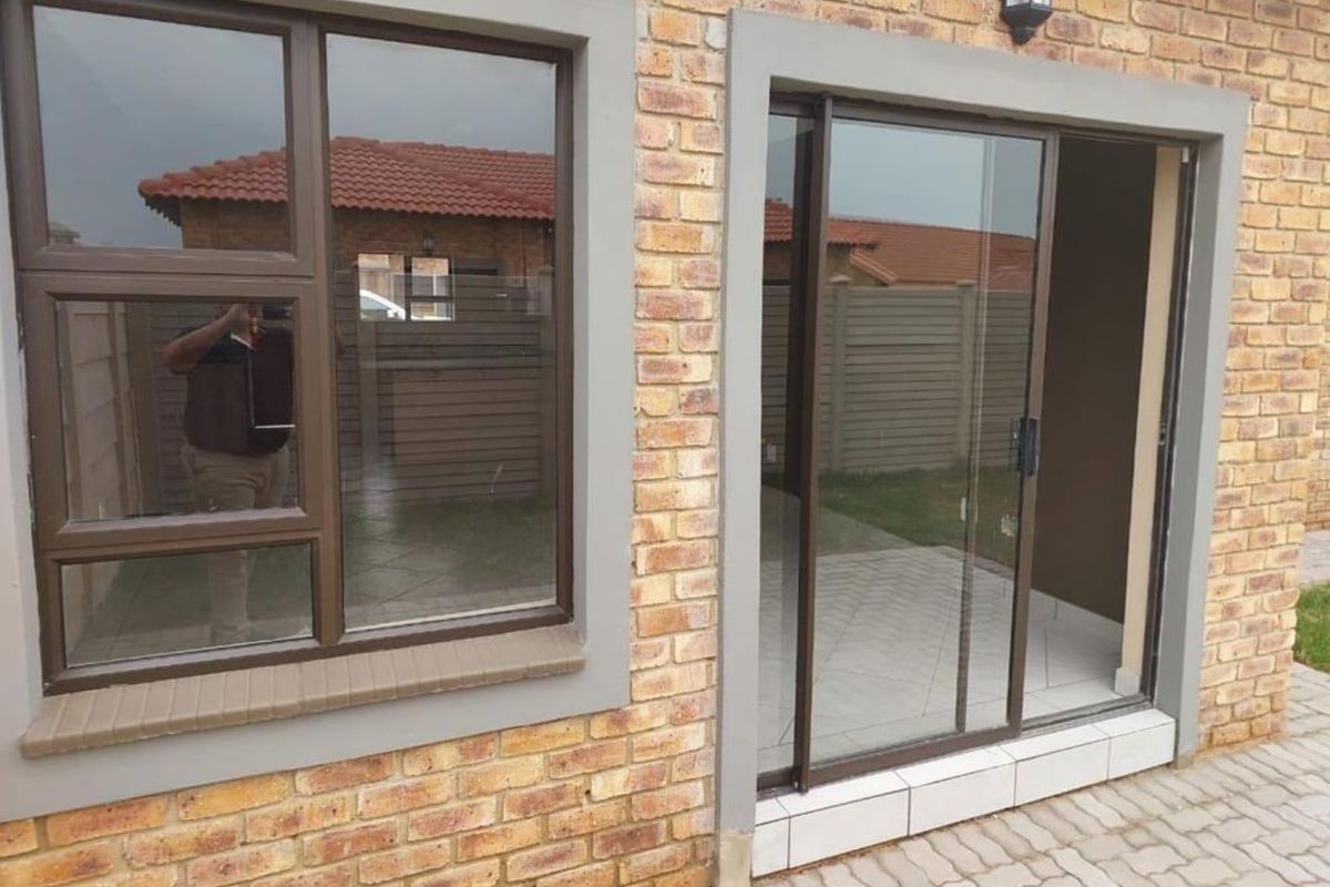 Exterior view of a townhouse featuring face-brick facade, aluminium-framed windows, and a sliding glass door leading to a paved patio area.