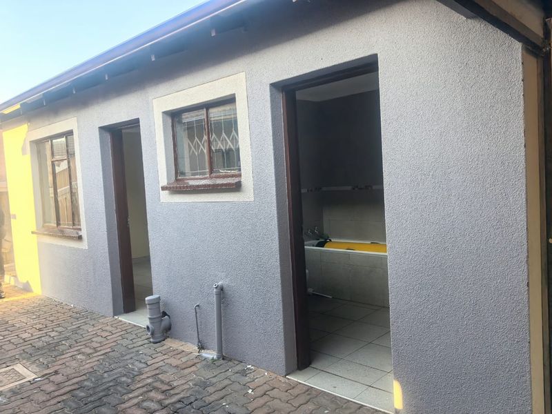 Rear exterior view of the property featuring a textured plaster facade, paved ground area, and access points to internal utility or bathroom spaces.
