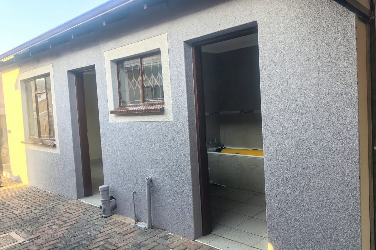 Rear exterior view of the property featuring a textured plaster facade, paved ground area, and access points to internal utility or bathroom spaces.