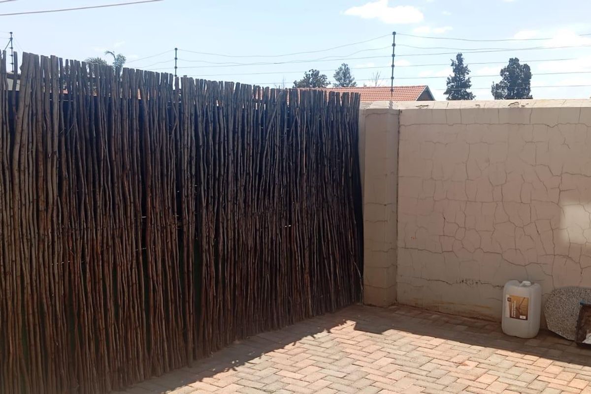 A private outdoor courtyard area featuring paved flooring, a high boundary wall with electric fencing, and a decorative reed privacy screen.
