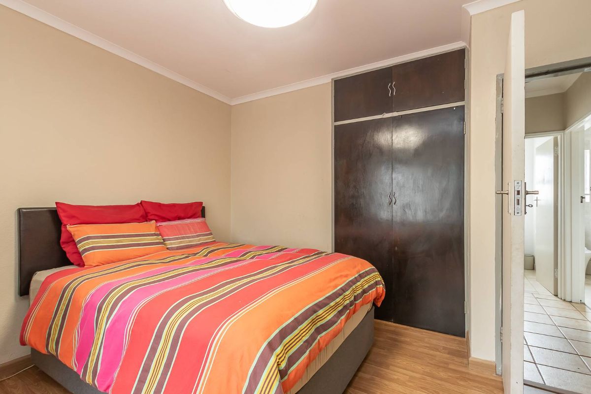 A bedroom featuring laminate flooring, a built-in wardrobe, and neutral wall tones, offering a functional space with potential for modern updates.
