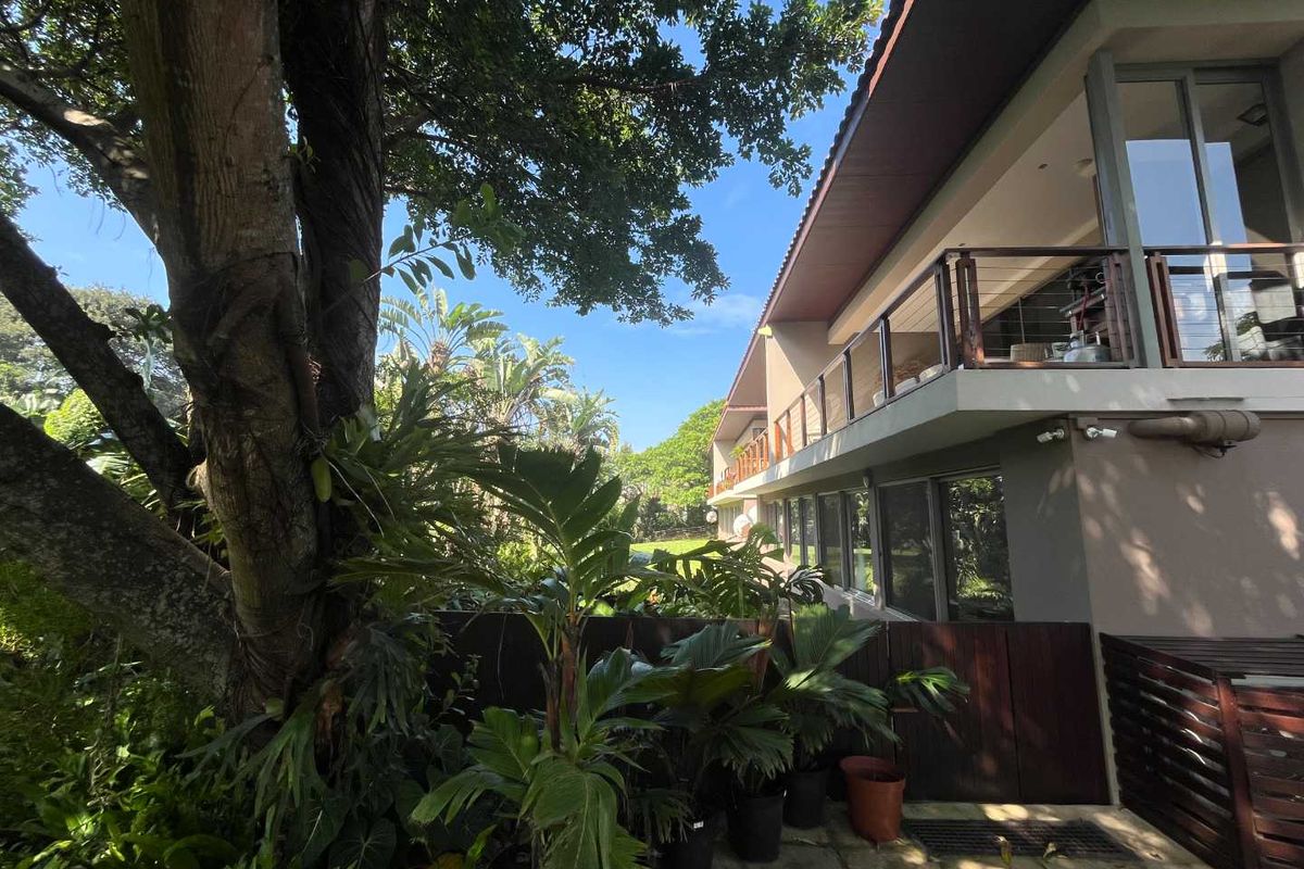 A view of the rear exterior of the apartment building, featuring a balcony with wooden railings and landscaped garden surroundings.