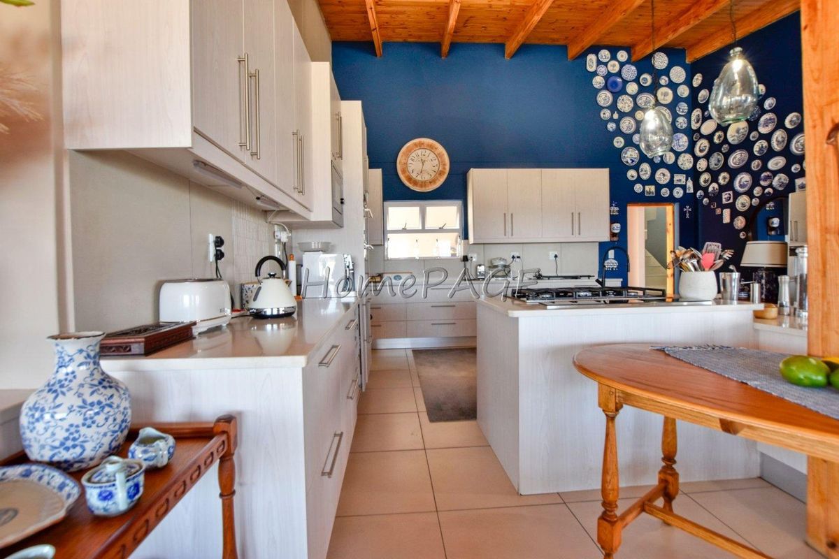 A well-lit kitchen featuring light-toned cabinetry, a central island with a built-in gas hob, tiled flooring, and a striking blue feature wall.