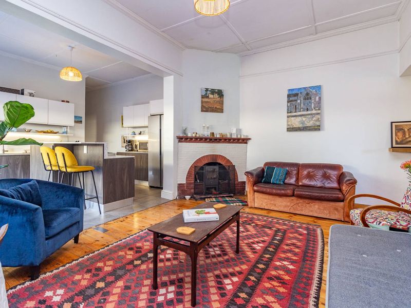 Open-plan living area featuring timber flooring, a classic brick fireplace, and a modern kitchen with island seating and contemporary cabinetry.
