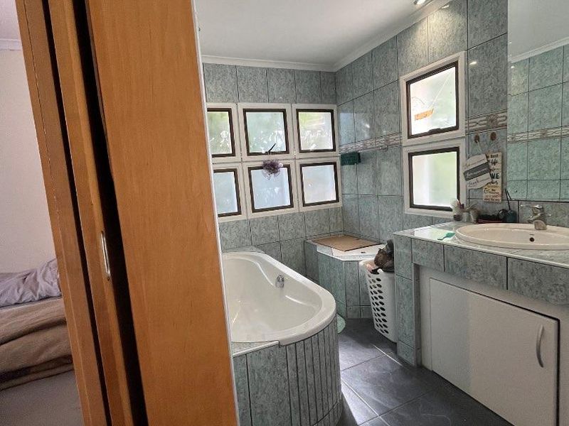 A functional bathroom featuring a built-in bathtub, vanity cabinet with integrated basin, and tiled finishes throughout, illuminated by recessed downlights.