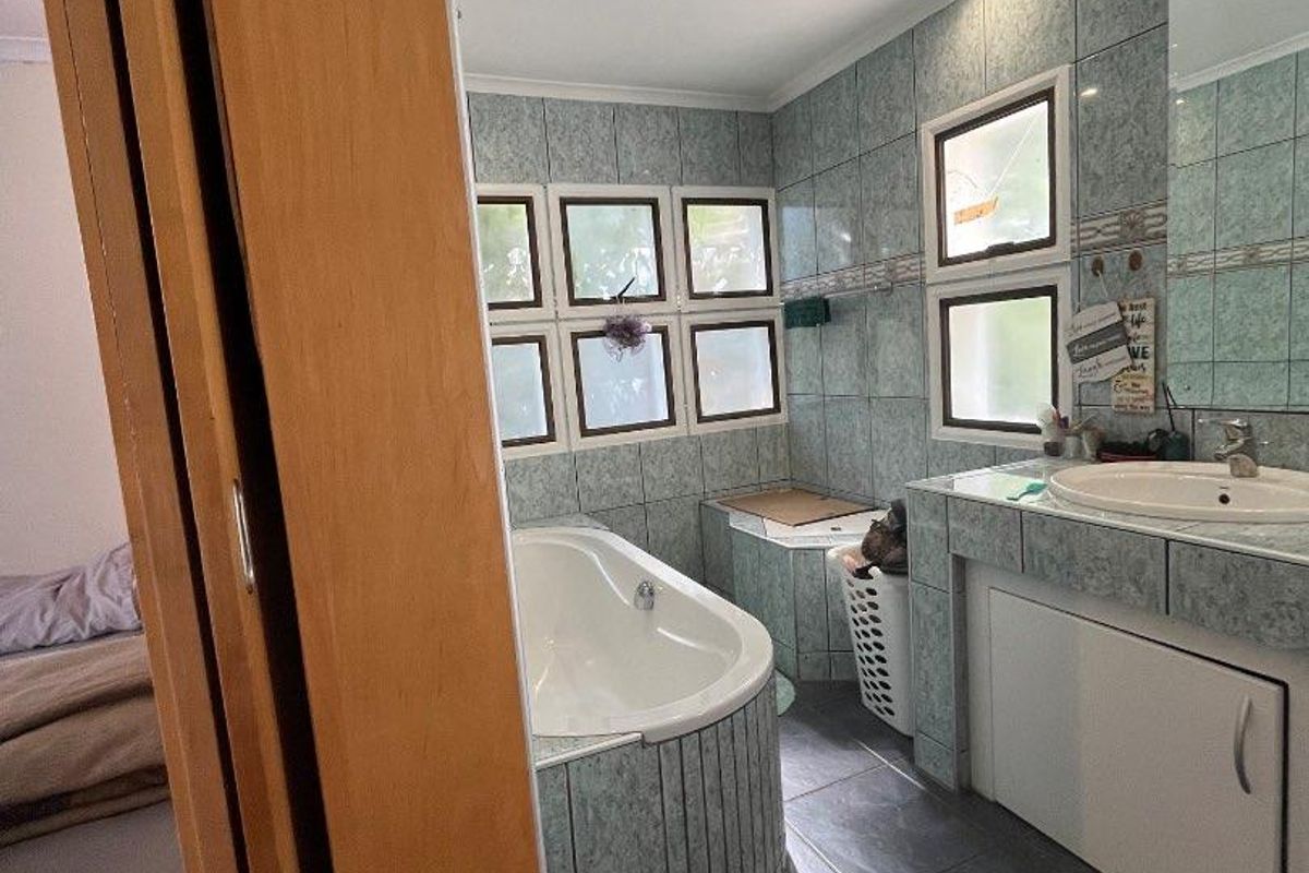 A functional bathroom featuring a built-in bathtub, vanity cabinet with integrated basin, and tiled finishes throughout, illuminated by recessed downlights.