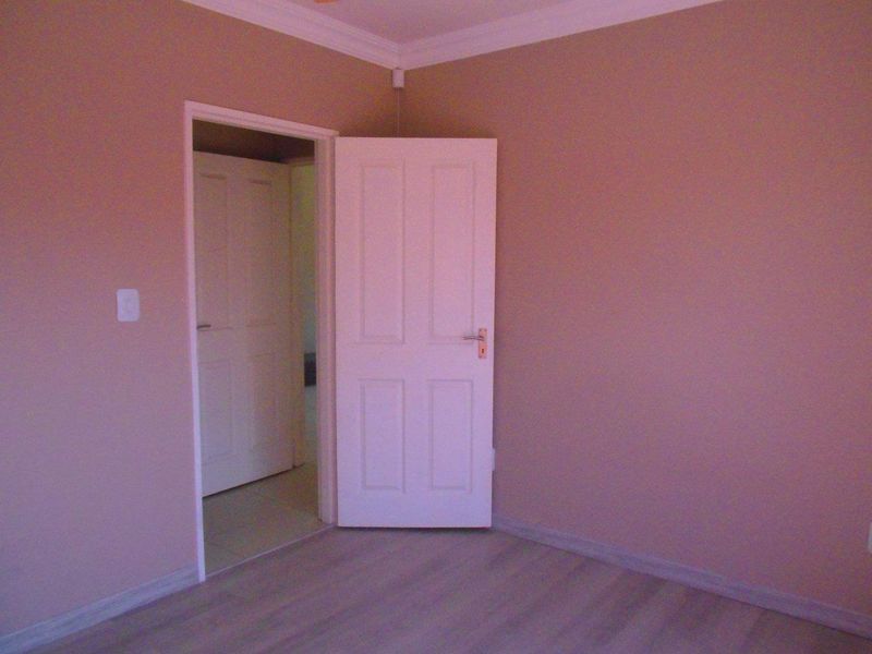 An empty bedroom featuring laminate flooring, neutral wall paint, and a classic panelled interior door with matching door frame.