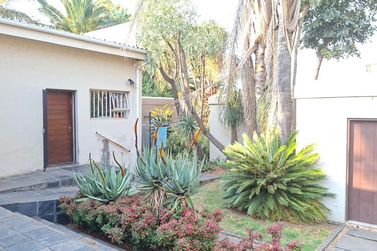 A rear exterior view featuring a paved courtyard area, established garden beds with succulents, and access to the main dwelling via a timber door.