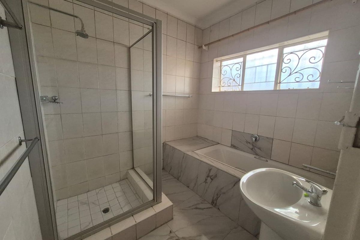 A functional bathroom featuring a glass-enclosed shower, a built-in bathtub with marble-look tiling, and a pedestal basin.