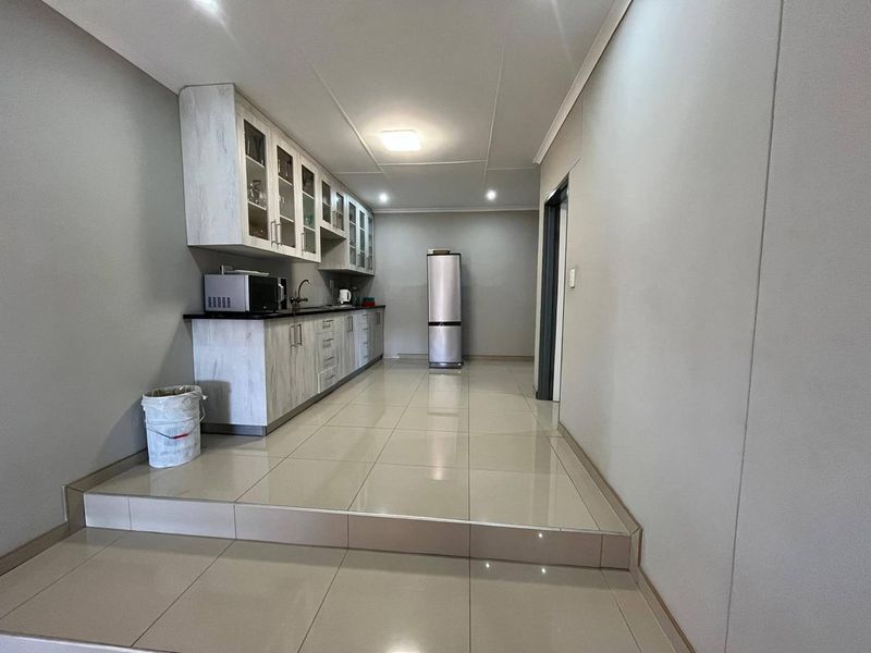 A functional kitchen area featuring built-in cabinetry, dark countertops, a sink, and neutral tiled flooring, elevated by a single step.