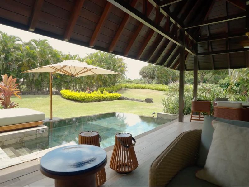 A covered outdoor patio area featuring a private swimming pool and views over a lush, well-maintained garden.