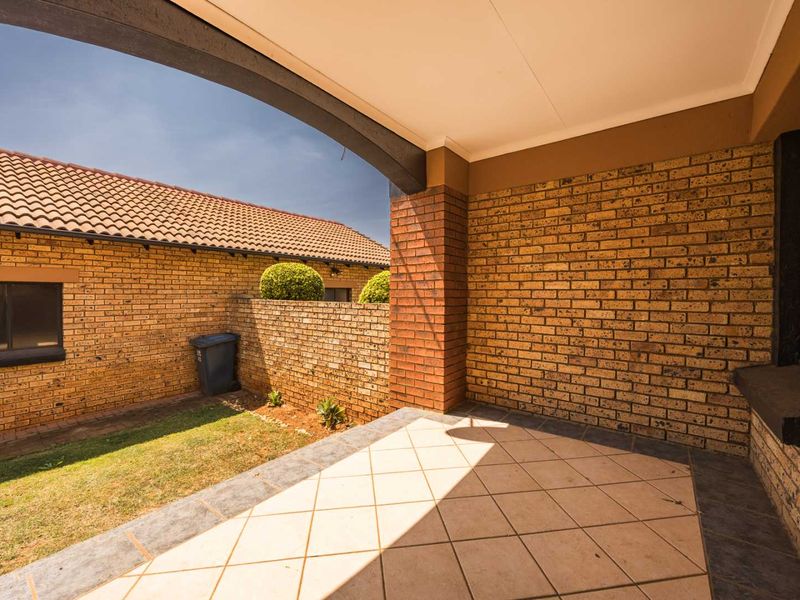 A covered patio area featuring face brick walls and tiled flooring, overlooking a small private garden space.