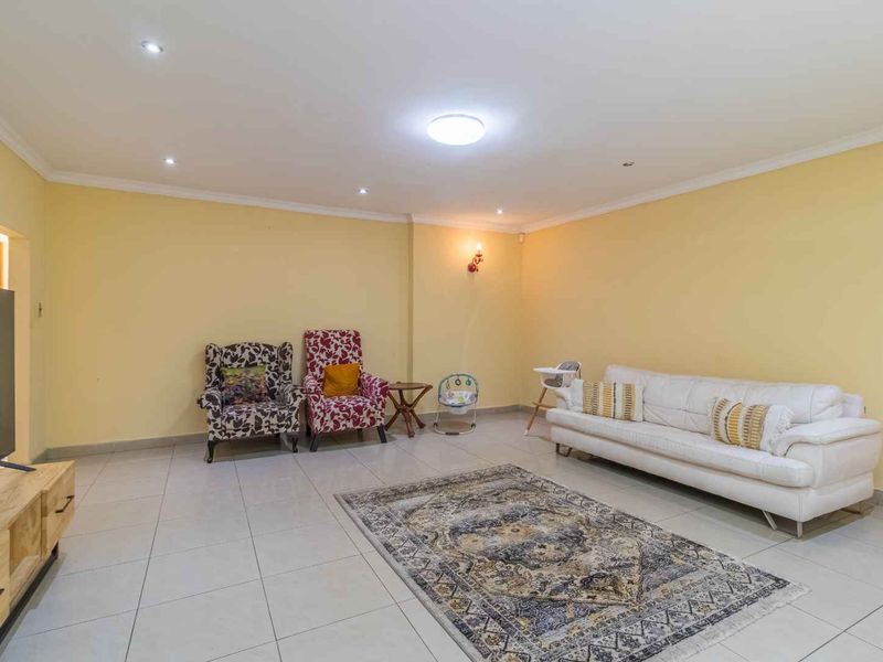 A spacious living room featuring neutral tiled flooring, recessed downlighting, and coved cornicing, providing a versatile area for relaxation and family gatherings.